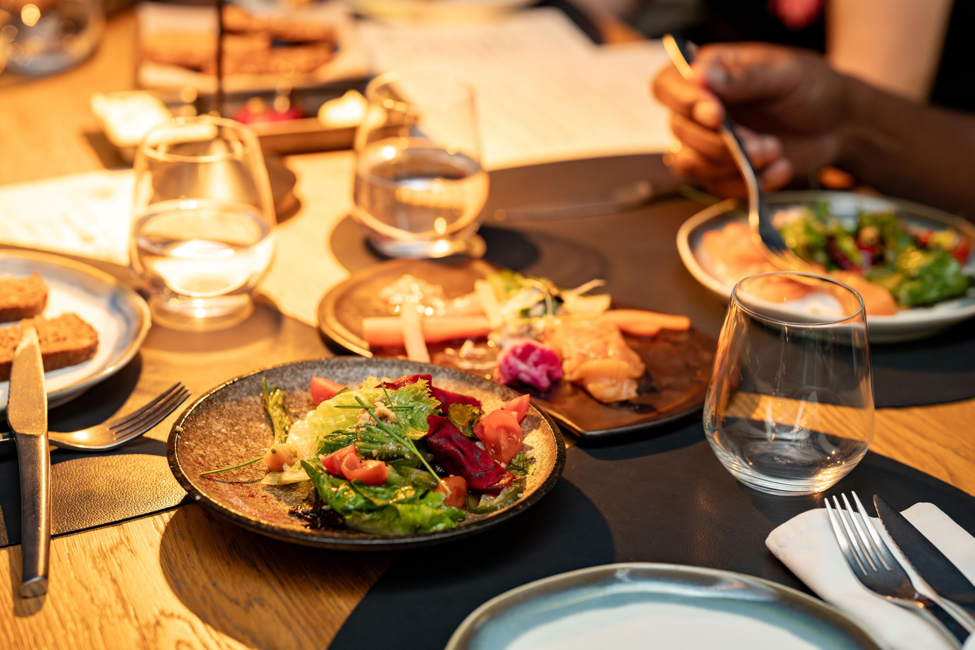 An overhead shot showcases an array of colorful plated dishes elegantly arranged on a dark wood table, illuminated by natural light, emphasizing the visual appeal of the food. This vibrant display could enhance a restaurant's website, attracting new customers with high-quality photos of seasonal menus and special events.