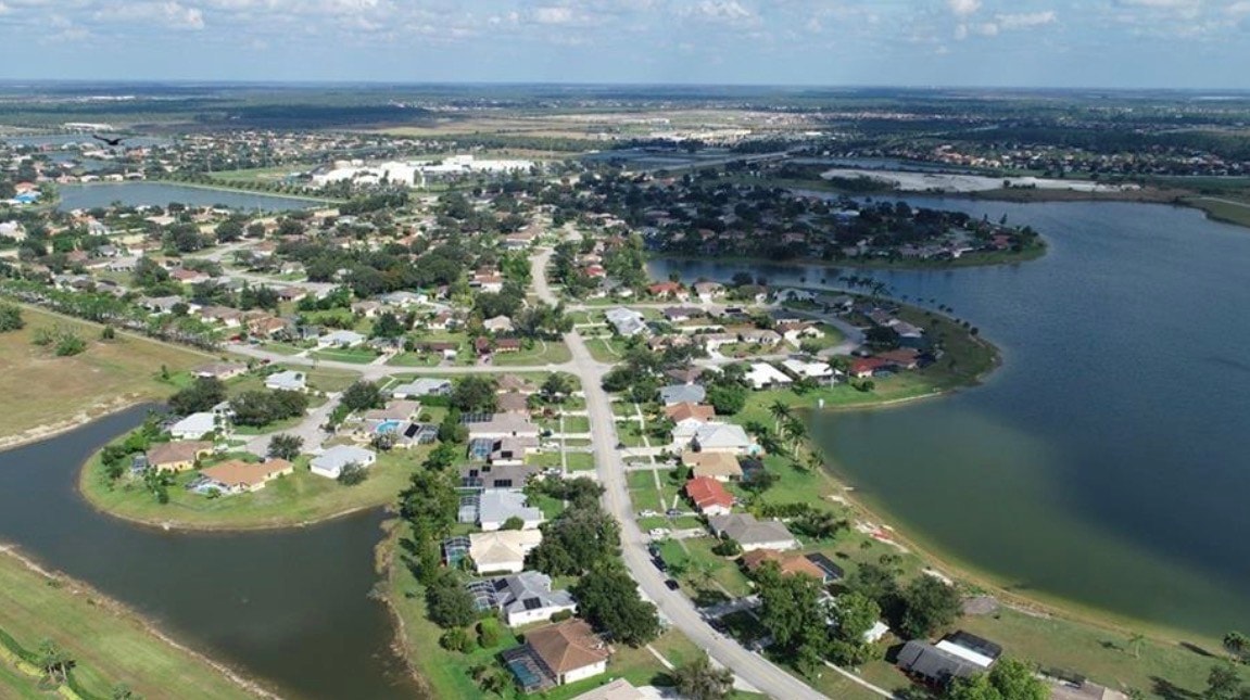 An aerial view of the tranquil Orange Tree community in Naples, Florida, showcases mature landscaping and serene lake views, highlighting the luxurious homes with spacious corner lots and immaculate pool homes. The community features resort-style amenities, including a community pool and jogging path, set against a backdrop of luscious trees and oversized yards.