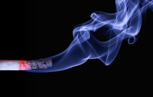 An image of a burning cigarette with smoke curling out from it on a black background.