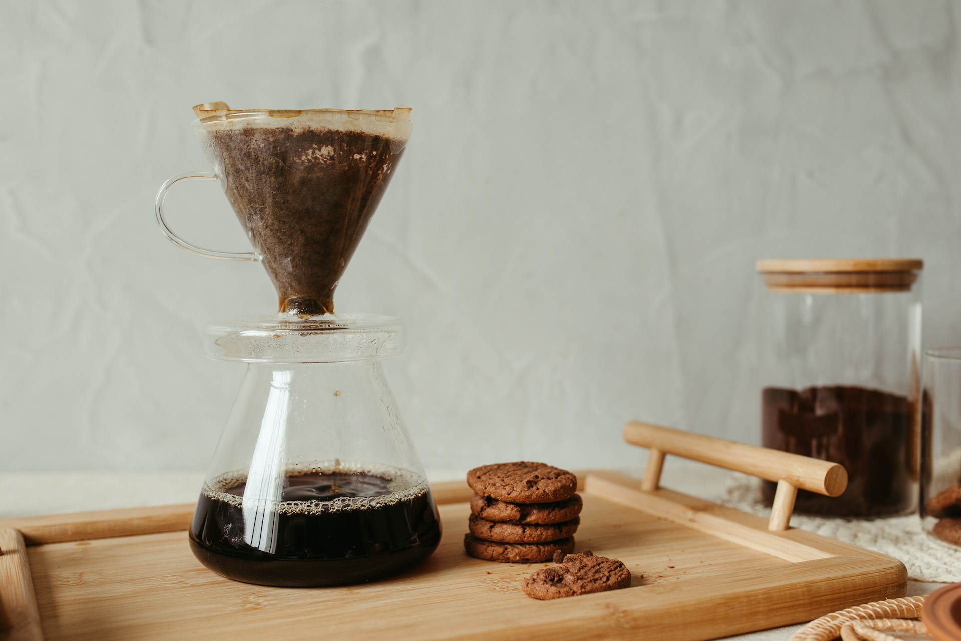 A pour over coffee cones on a wooden tray next to chocolate cookies