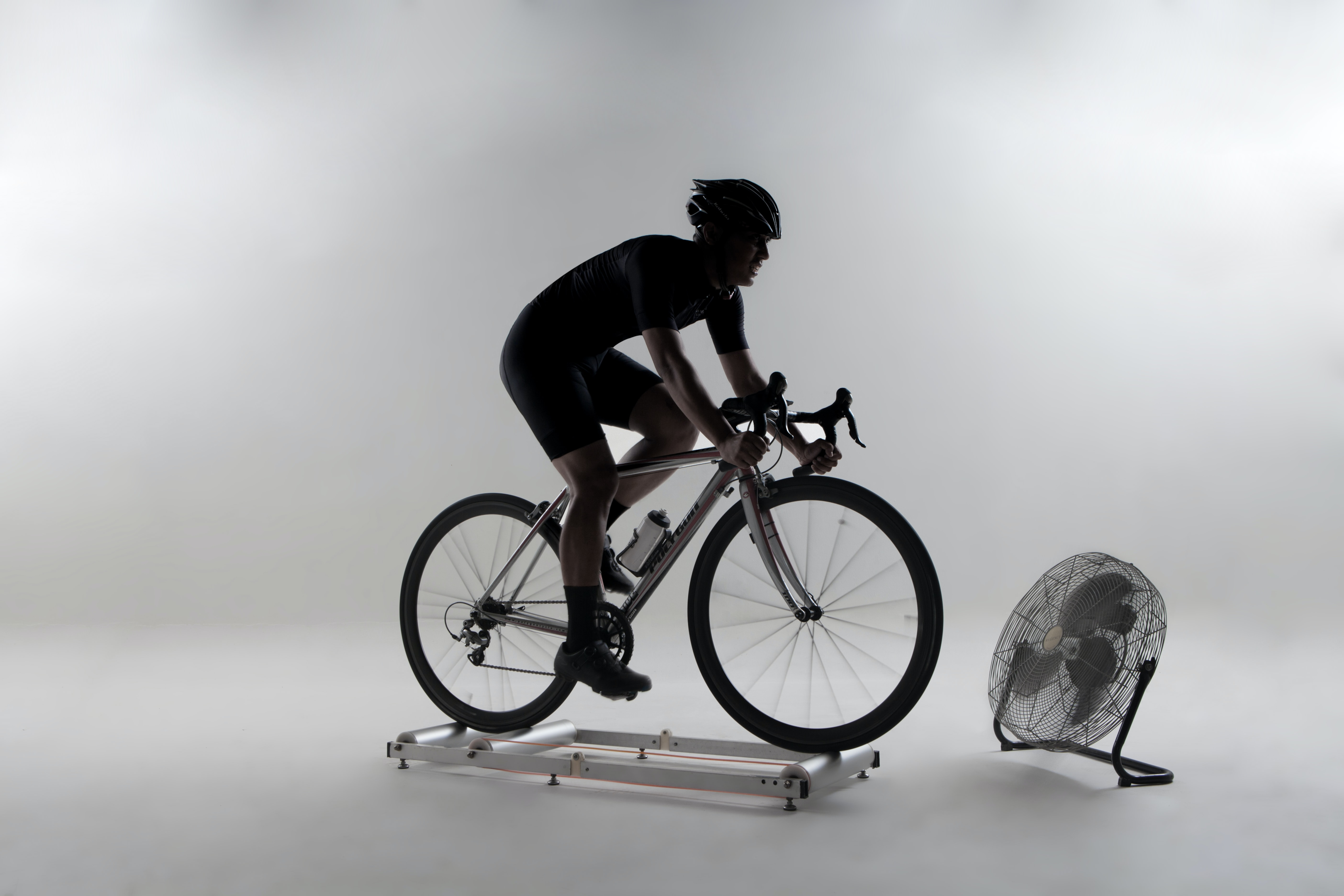 Ciclista utilizando um rolo de treino para bike, com um ventilador para ajudá-lo a se refrescar
