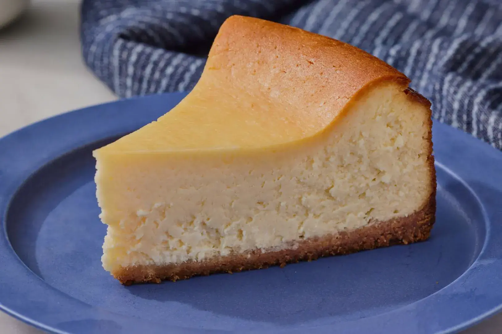 A slice of creamy new york cheesecake on a blue plate with a textured background.