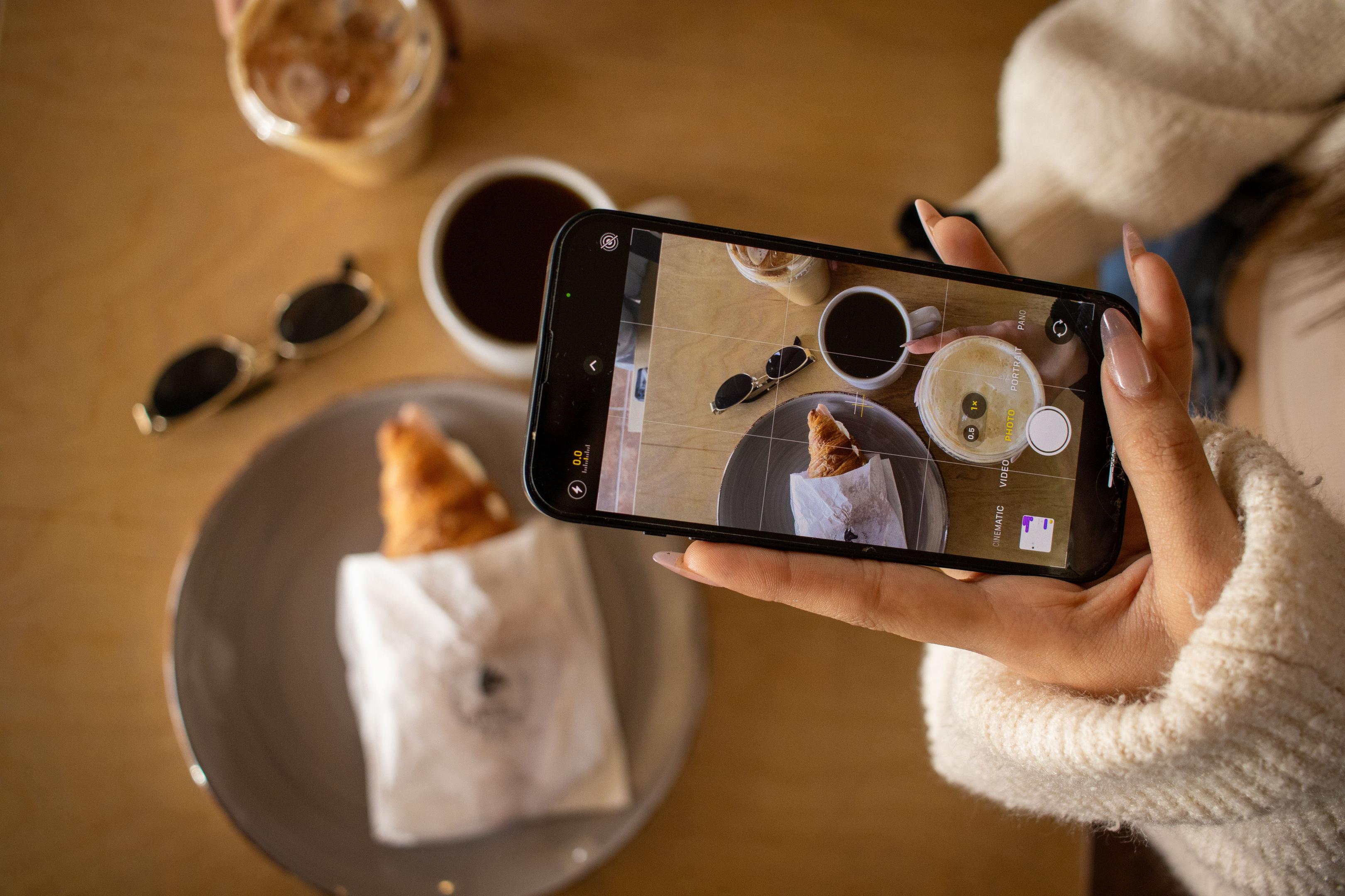 A woman takes a picture of her morning coffee and pastry.