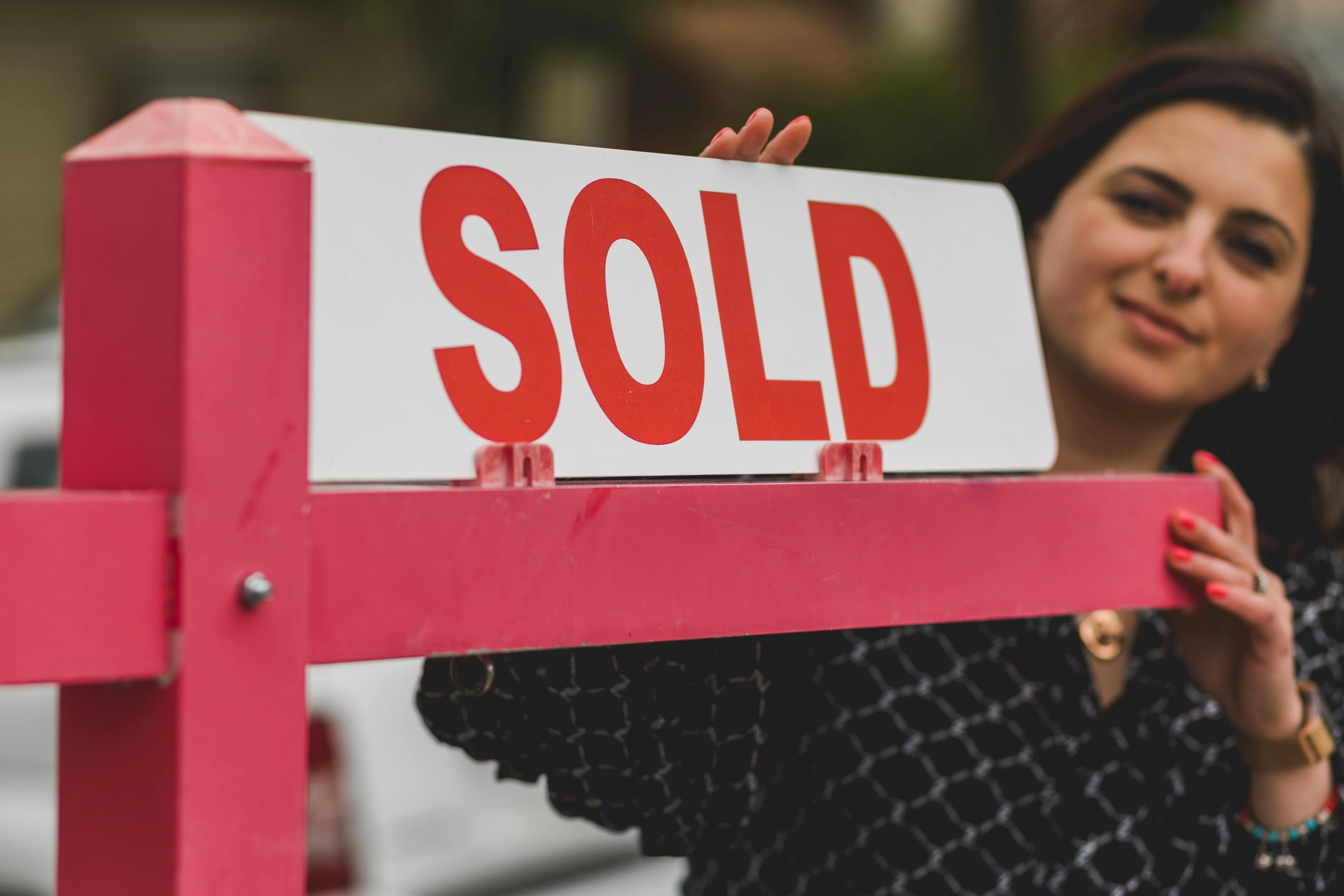 Real estate investor next to 'Sold' sign in front of property she purchased.