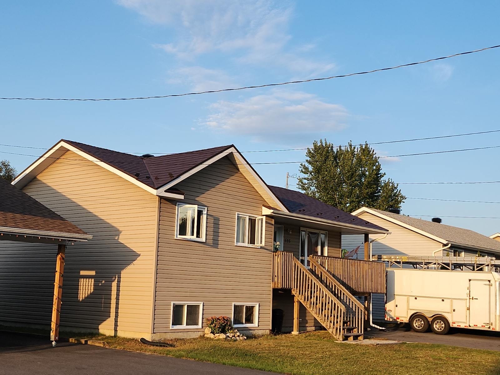 A home with a dark metal roof, light brown siding and a small balcony with descending stairs which lead to the driveway.