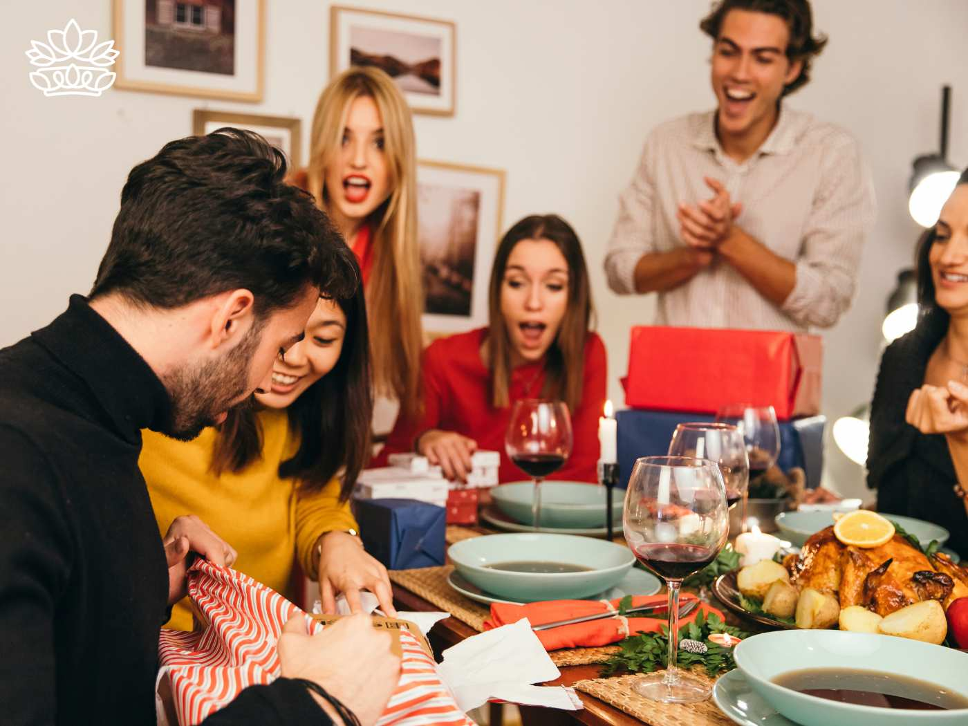 Friends gathered around a festive dinner table enjoying a surprise gift, part of the Festive Season Collection delivered with heart by Fabulous Flowers and Gifts. This scene captures a country-wide tradition where people from various parts of the world tend to attend online parties, discovering joy in giving presents, expected to be sold extensively, providing access to happiness without spending much money among strangers.