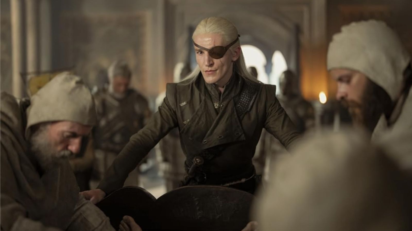 Ewan Mitchell as Aemond Targaryen with eyepatch leans over table commanding attention from soldiers in House of the Dragon Season 2
