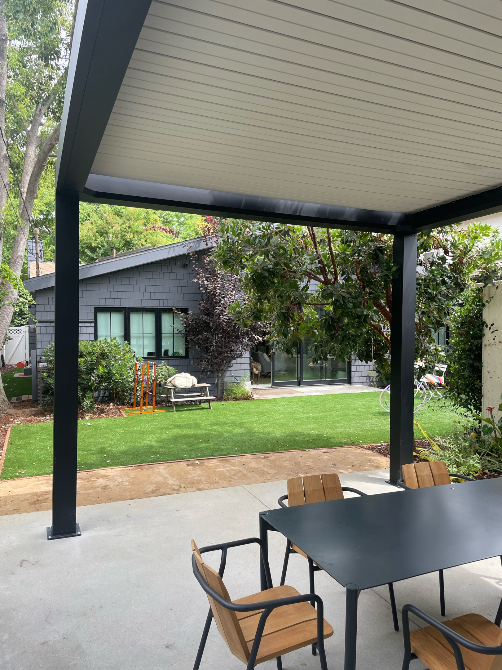 Dining table on patio with greenery on back wall with clean lines showing closed louver roof on pergola.