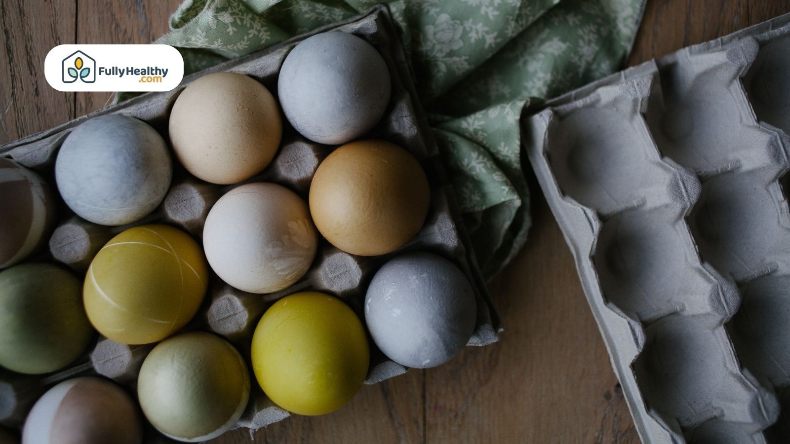 Assorted colored eggs in carton on wooden table with green cloth