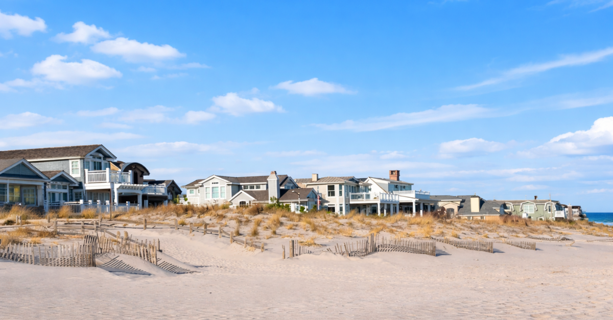 Image of oceanfront homes behind sand dunes in Avalon, New Jersey with a wide sandy beach and blue summer sky