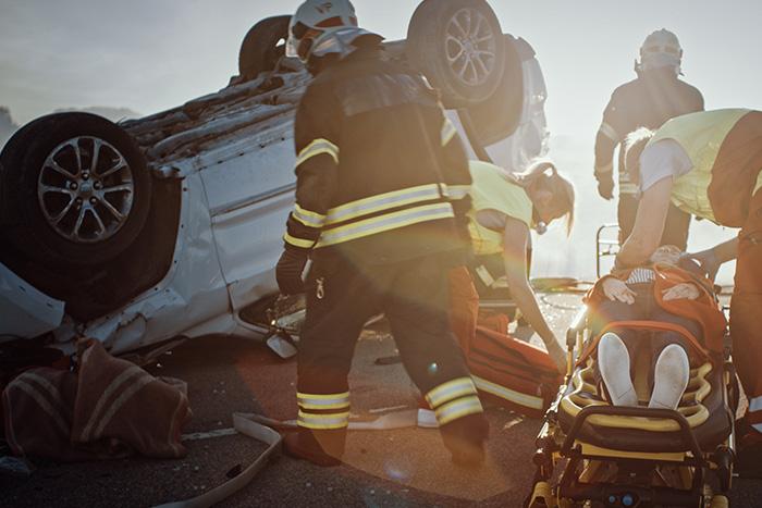 Emergency responders and paramedics assisting injured victim on stretcher at rollover car accident scene