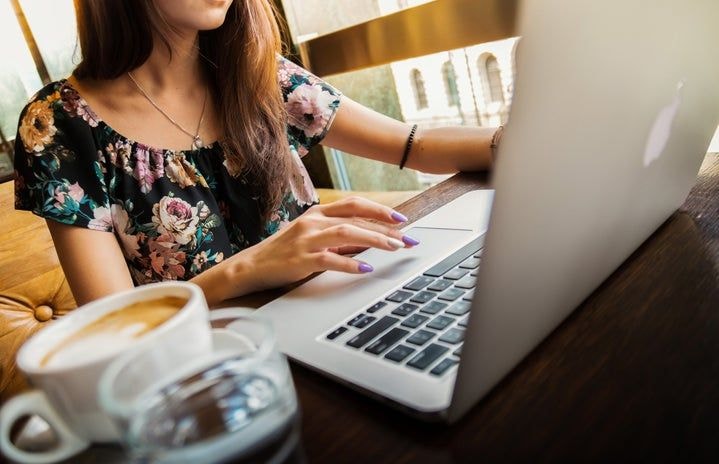 Kobieta pracuje na laptopie Apple w kawiarni. Na stole jest woda i kawa.