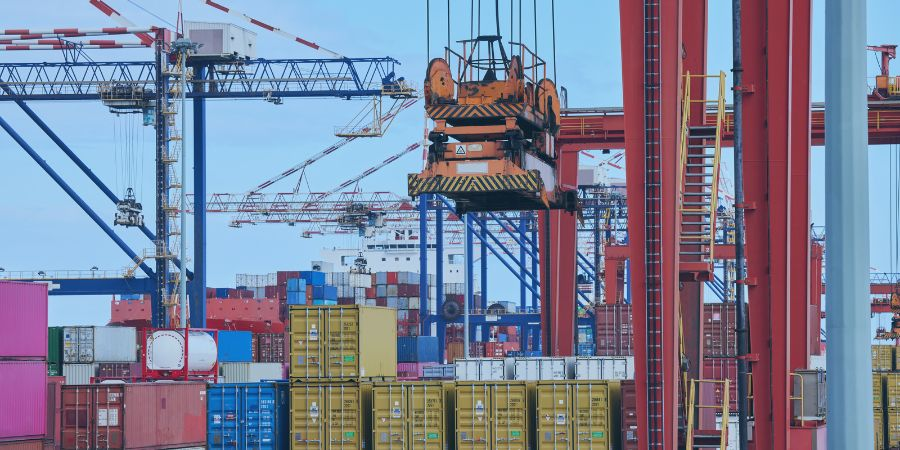 Cargo containers being loaded and unloaded at a busy shipping port with cranes in operation.