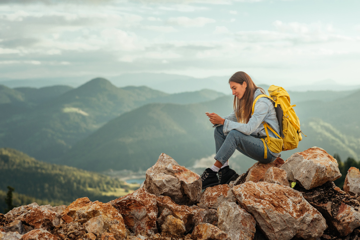 Young woman sitting on a hilltop checking her messages.