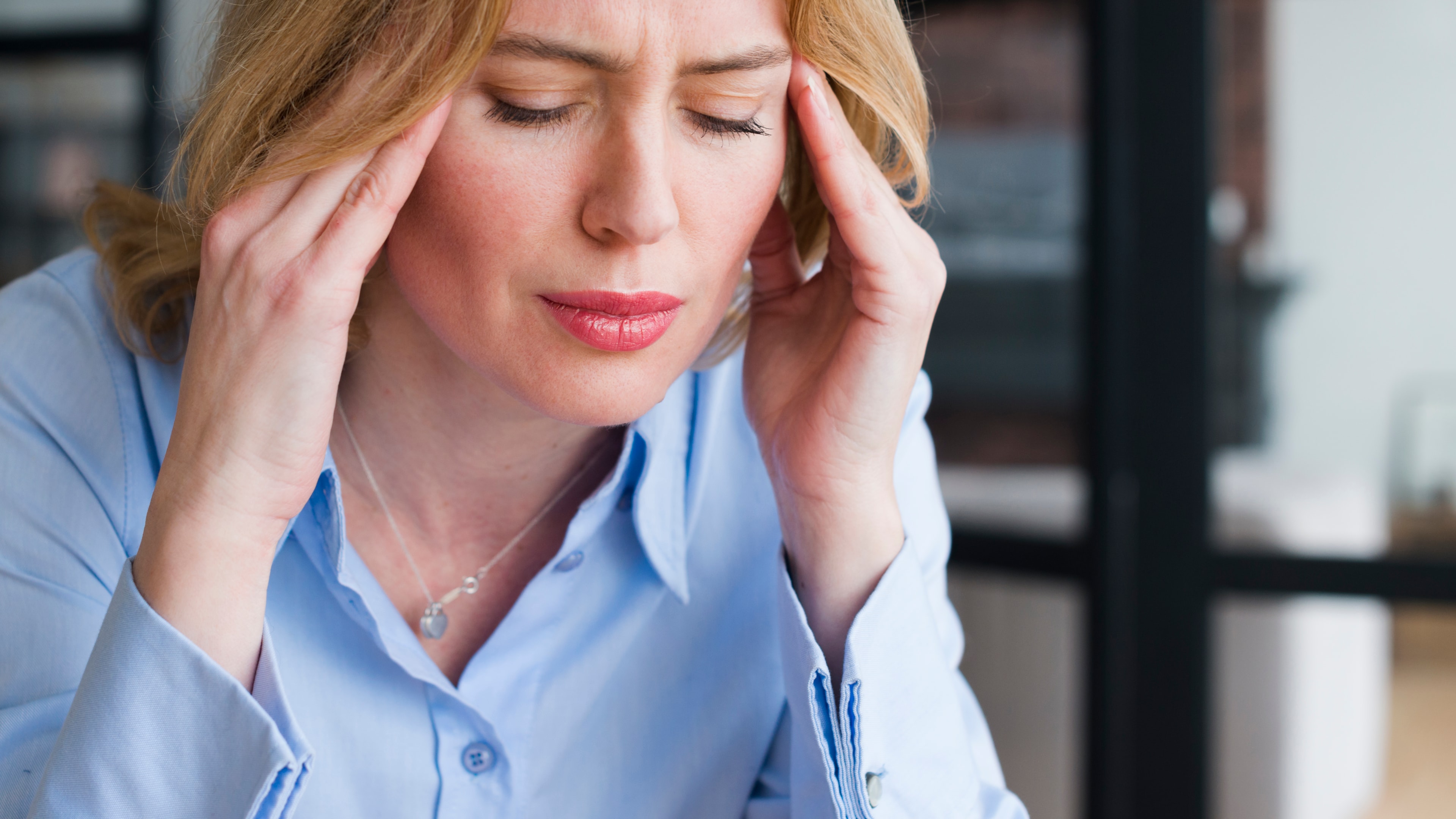 Blonde female feeling pain while holding her head