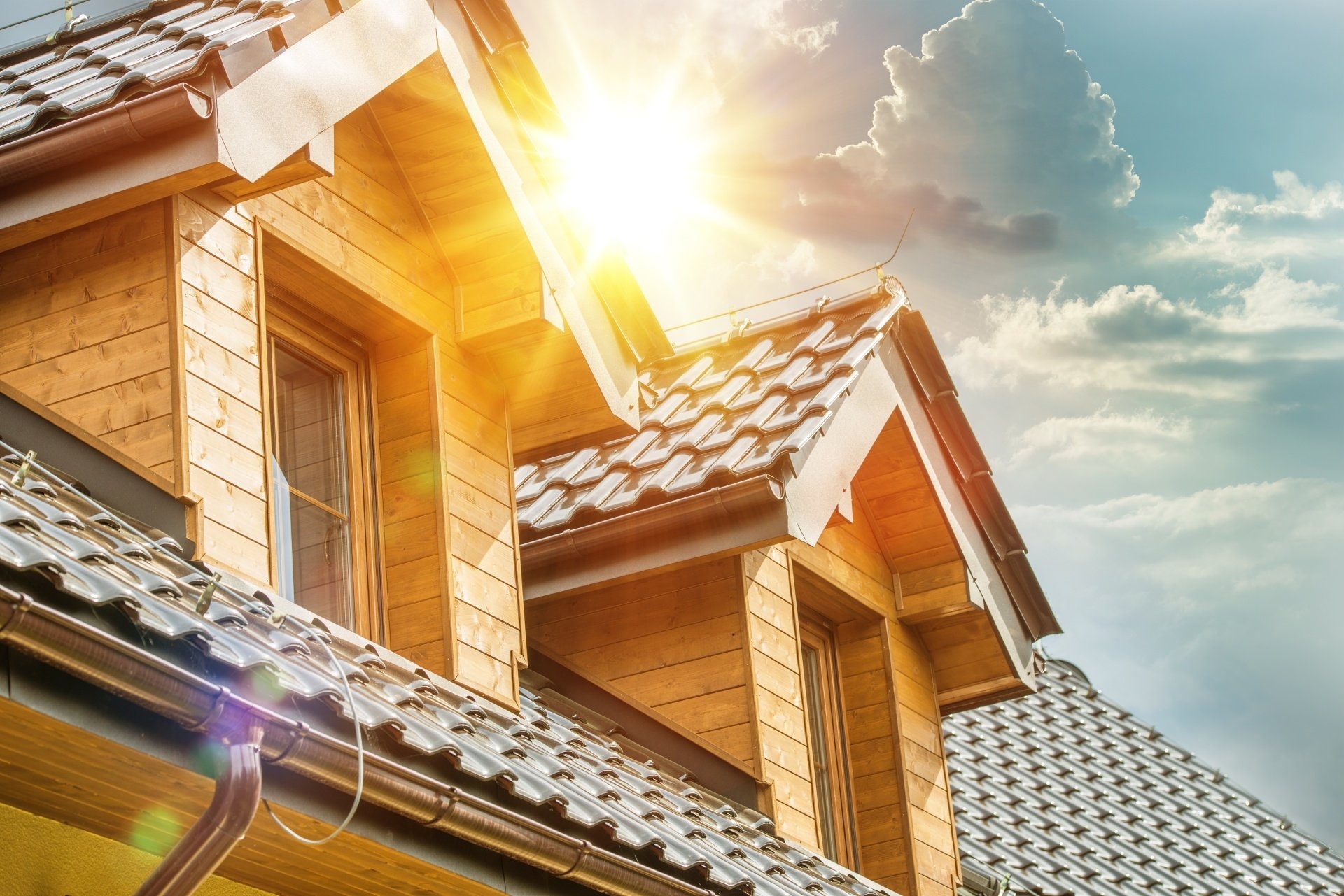 A picture of the sun shining on residential metal roofs, with a blue sky and clouds in the background.