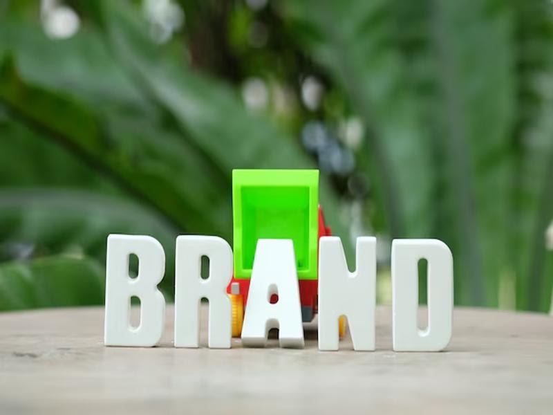 An arrangement of white letters spelling "BRAND" with a construction vehicle positioned behind them, symbolizing the process of building a brand.