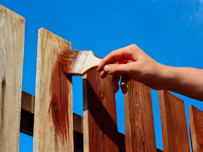 An image showing a professional repairing a fence while a homeowner works on a minor fence repair.