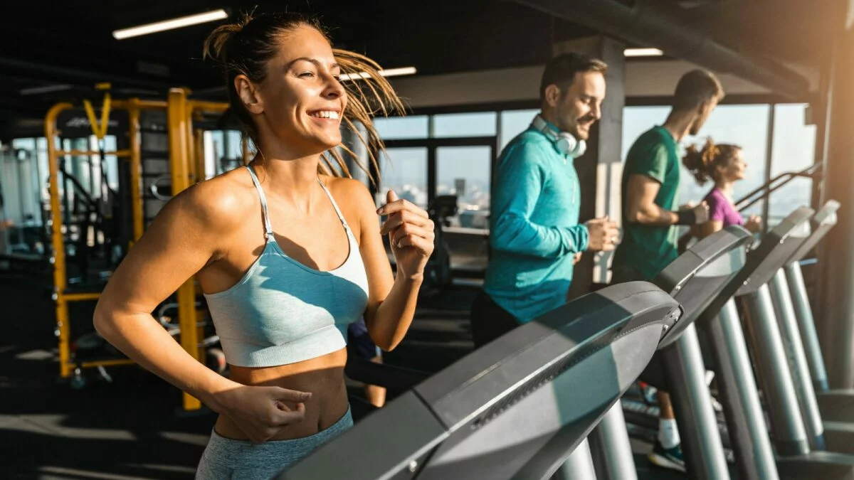 Na imagem: dois homens e duas mulheres fazendo exercício físico na academia.