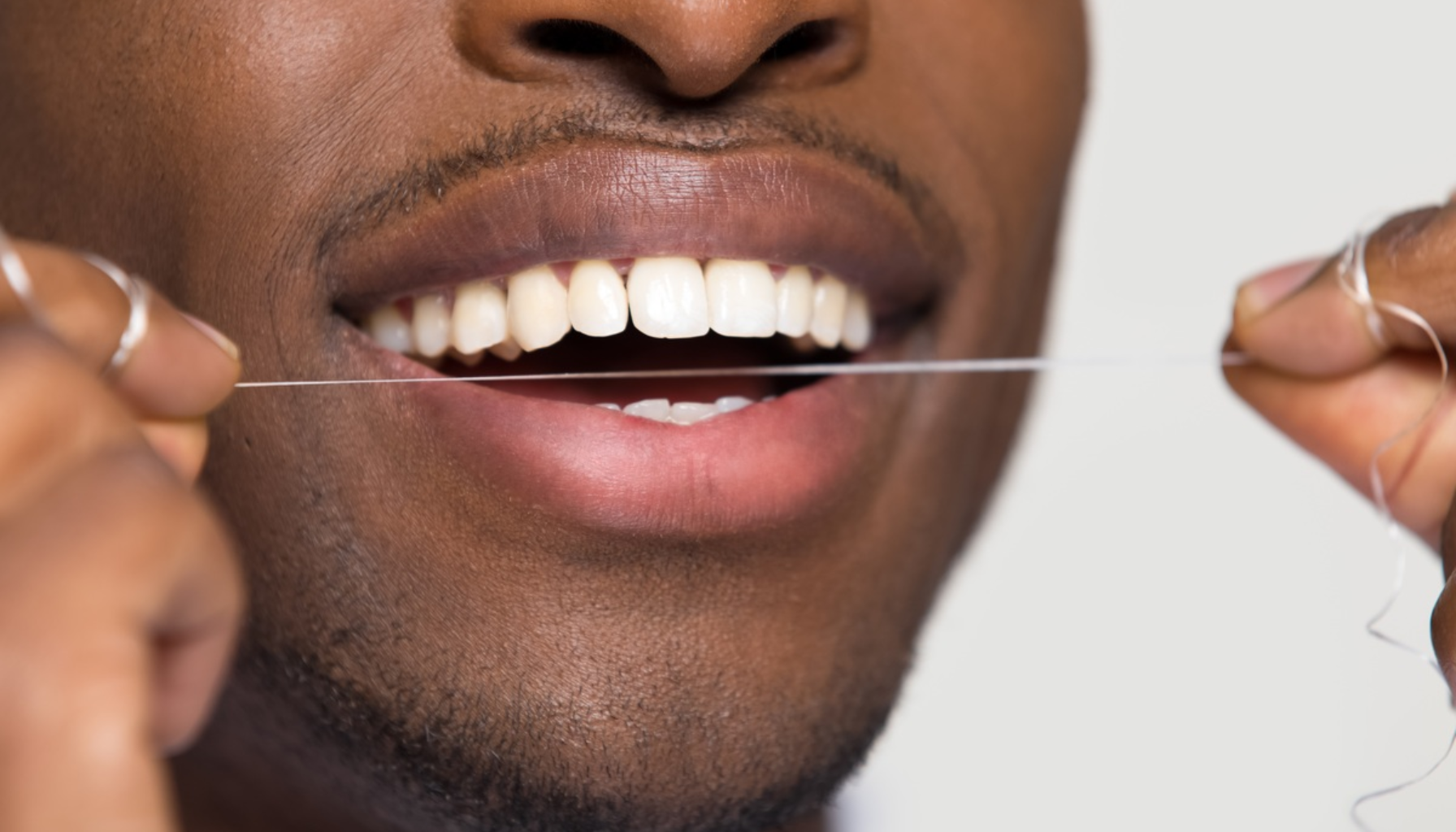 Nærbilde av mann som smiler mens han bruker tanntråd mellom tennene for god munnhygiene.