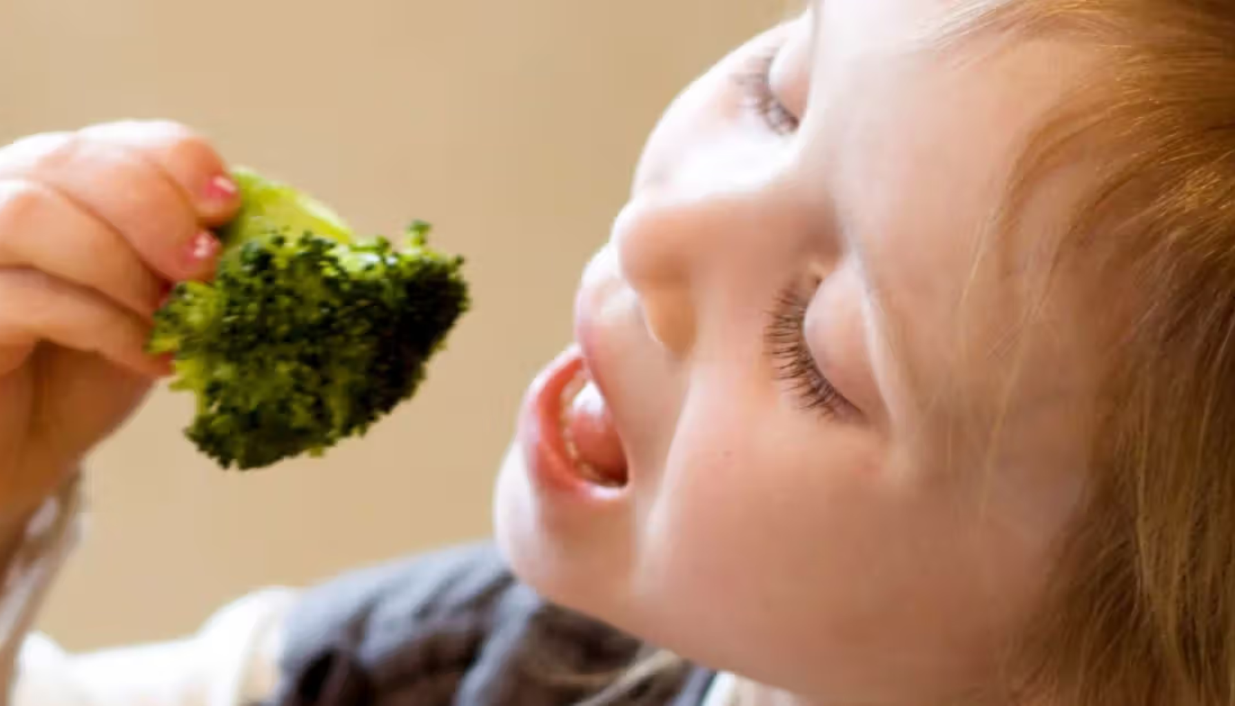 Kalsium – Derfor trenger kroppen din dette mineralet 11 Lite barn med lyst hår spiser brokkoli med glede, holder den opp til munnen og smiler mens hun tar en bit.