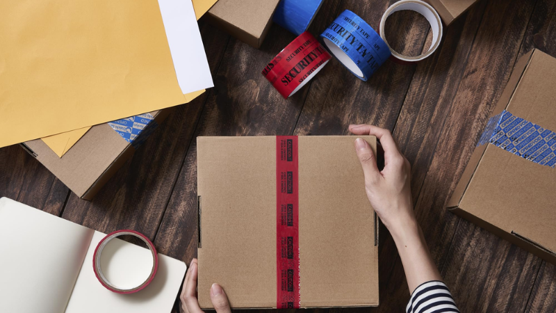 Tamper-evident red security tape sealing a cardboard box with packaging materials nearby