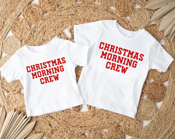 two white Christmas outfits with red block print spelling out "Christmas Morning Crew" against a woven rug