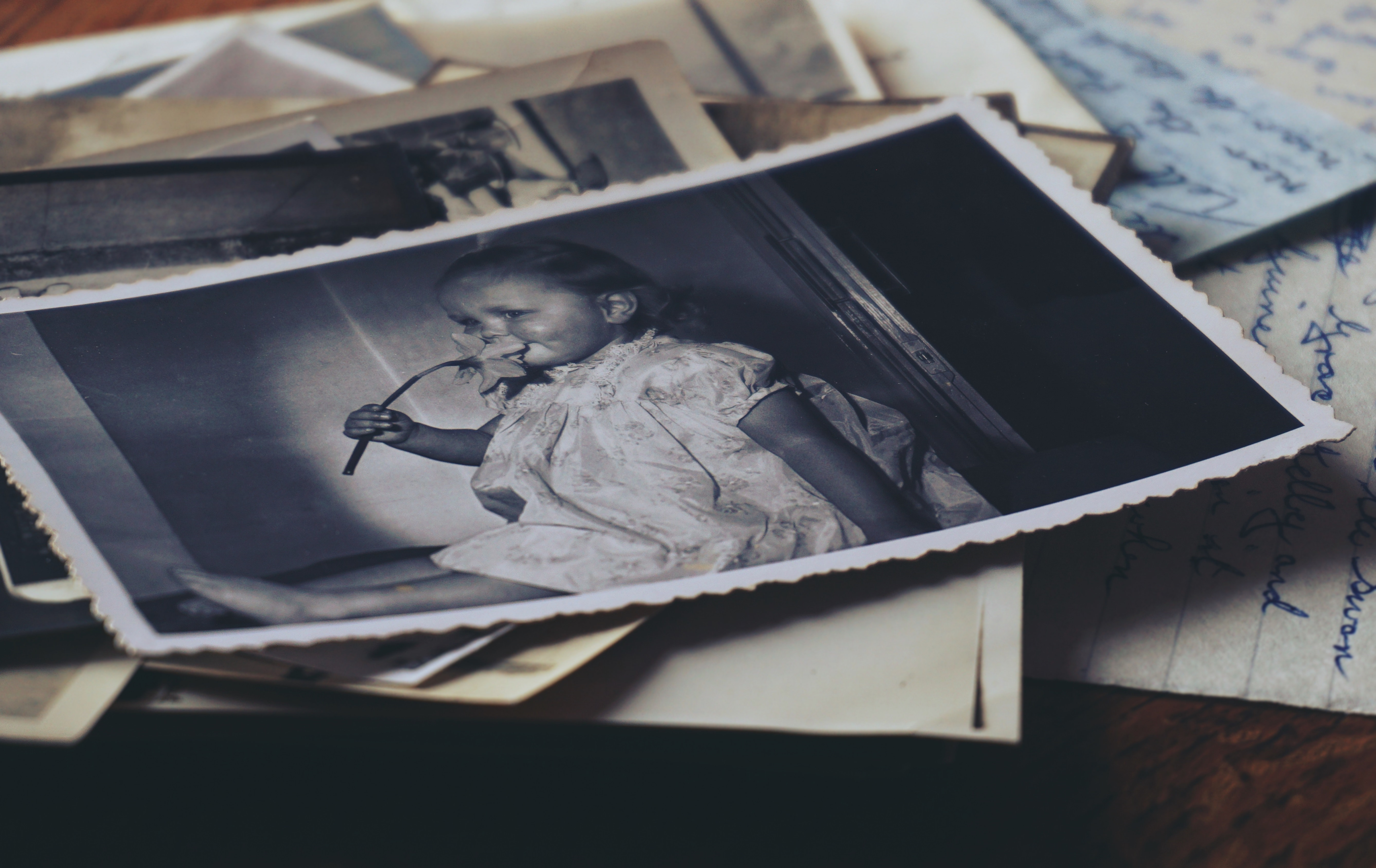 An old black and white photo of a little girl in a dress smelling a flower. Underneath, there are some other photos that seem damaged. With inpainting, these photos can be restored.