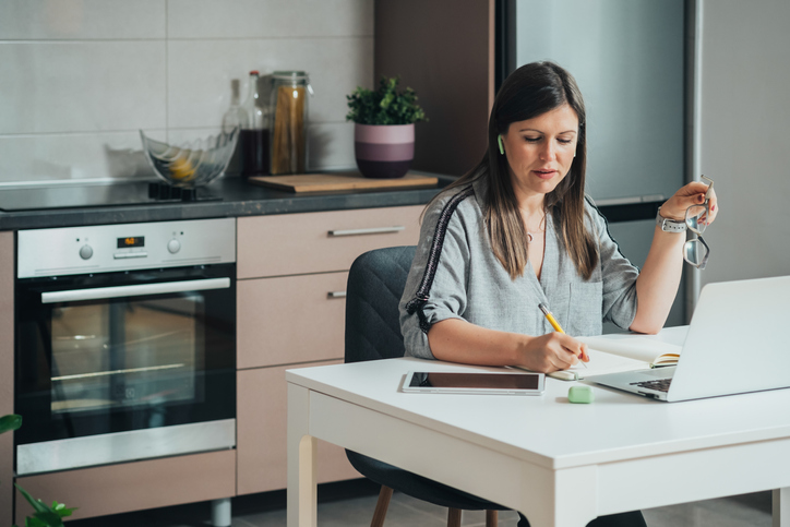 Woman working at the kitchen table with her earbuds in. 