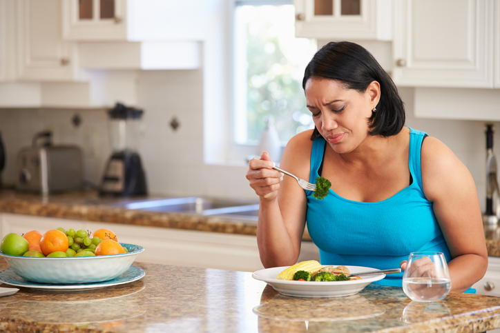 An image of a woman grimacing at her next bite of food, as she knows it tastes bad.