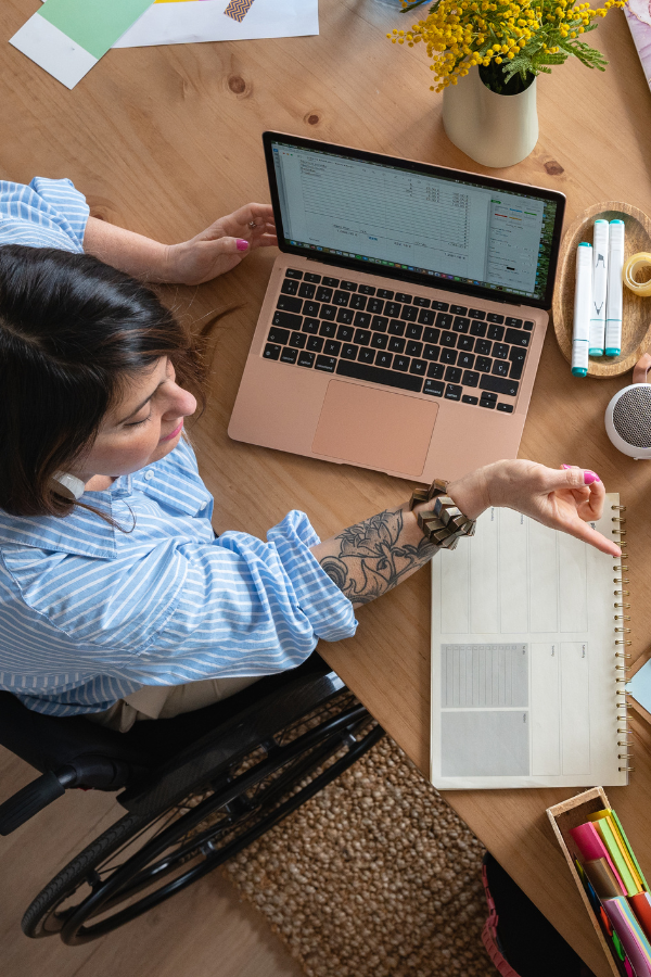 woman in a wheelchair at her desk conducting online research on her pink laptop