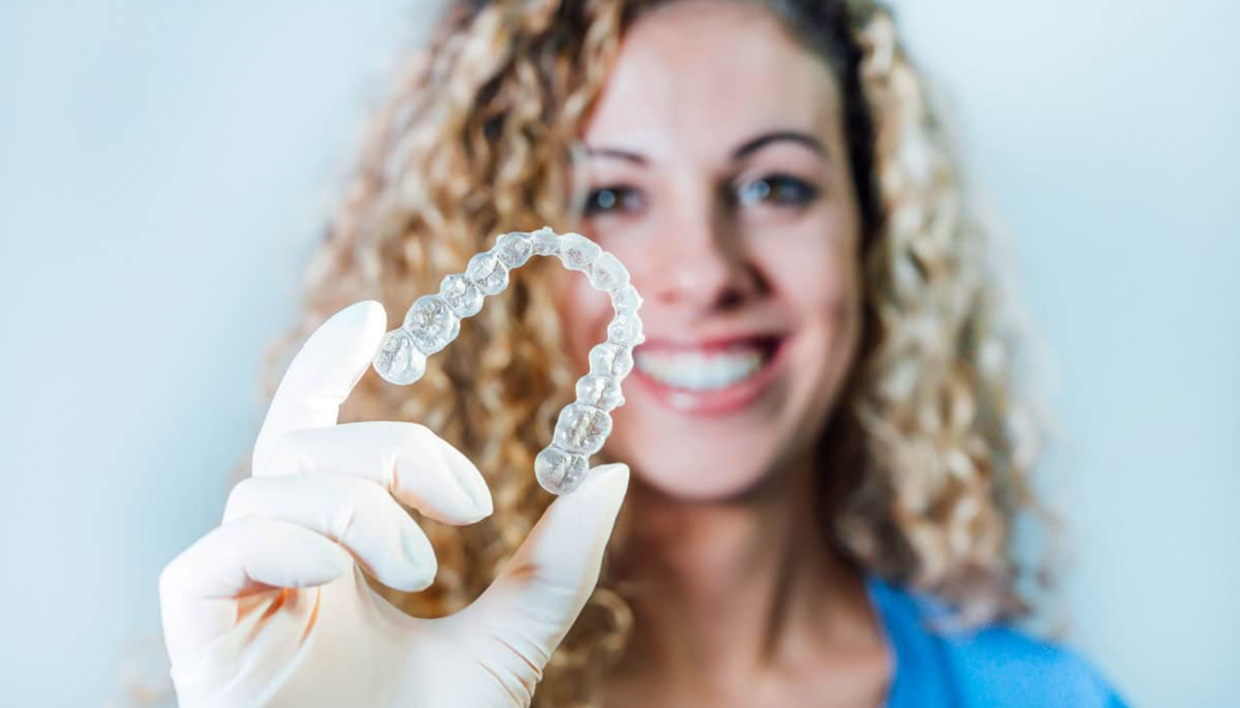 Invisalign – Usynlig tannregulering for voksne og ungdom 3 Smilende kvinne holder opp en gjennomsiktig tannskinne.