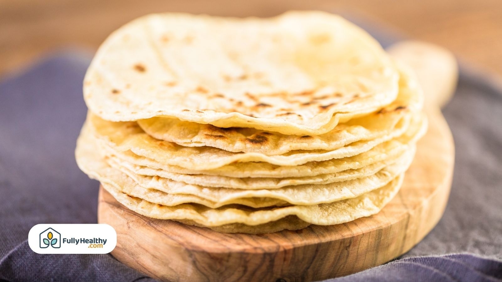 Stack of freshly cooked tortillas on a wooden board, with grill marks visible
