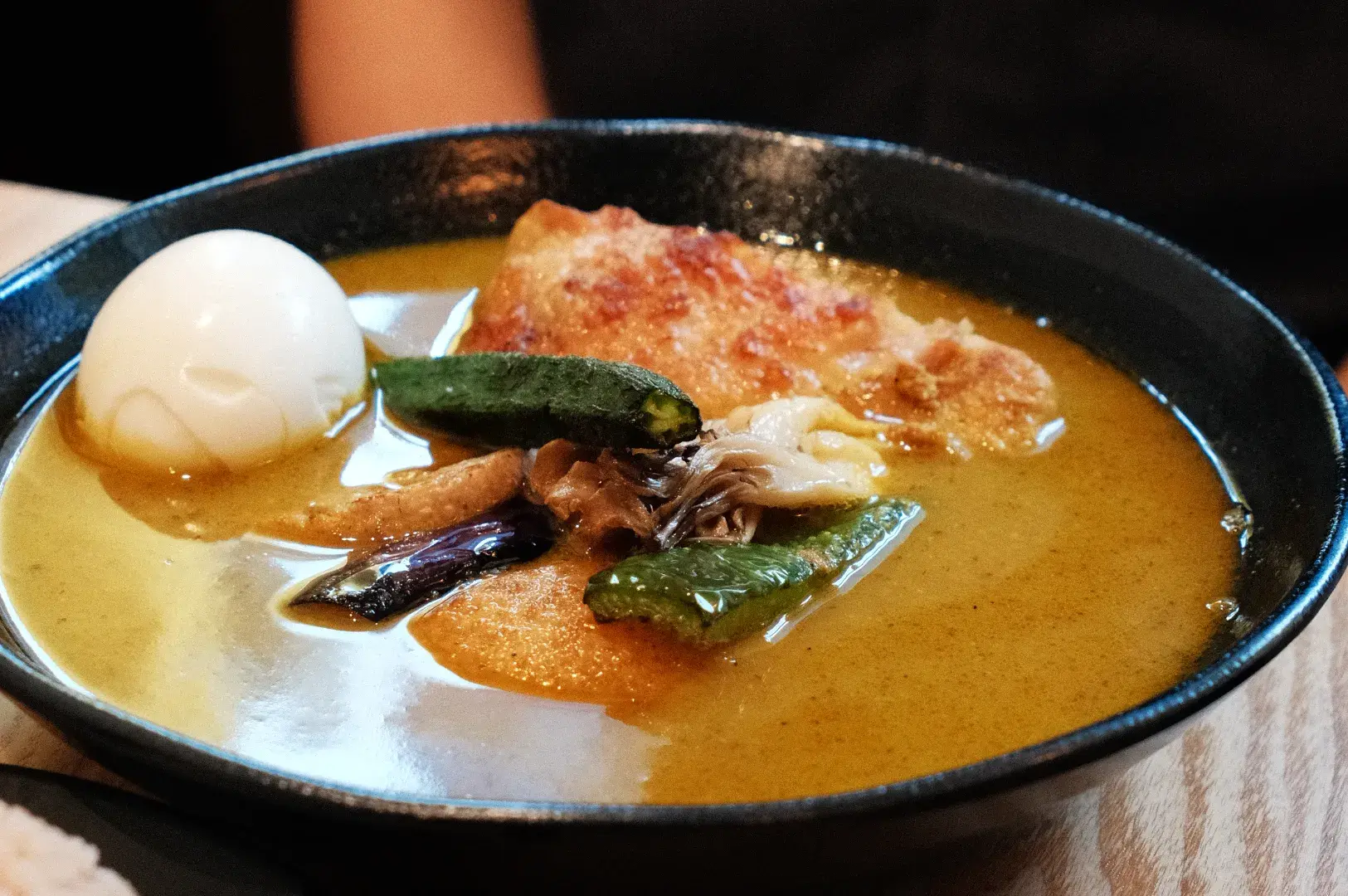 A bowl of ramen with a creamy yellow broth, topped with a boiled egg, chicken, and various vegetables.