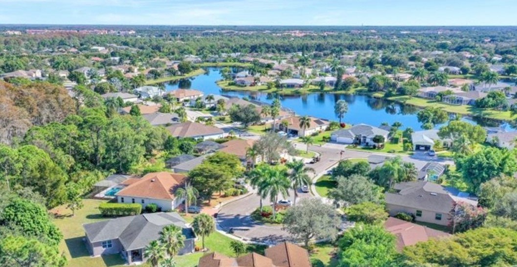 The image shows a street view of Coconut Road, highlighting easy access to the desirable Meadowbrook community in Estero, Florida. The scene features well-maintained sidewalks and lush landscaping, suggesting a welcoming environment for residents and visitors alike.
