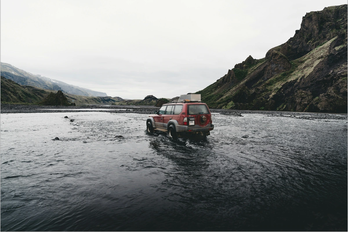 Red four wheel drive fording a river in Iceland