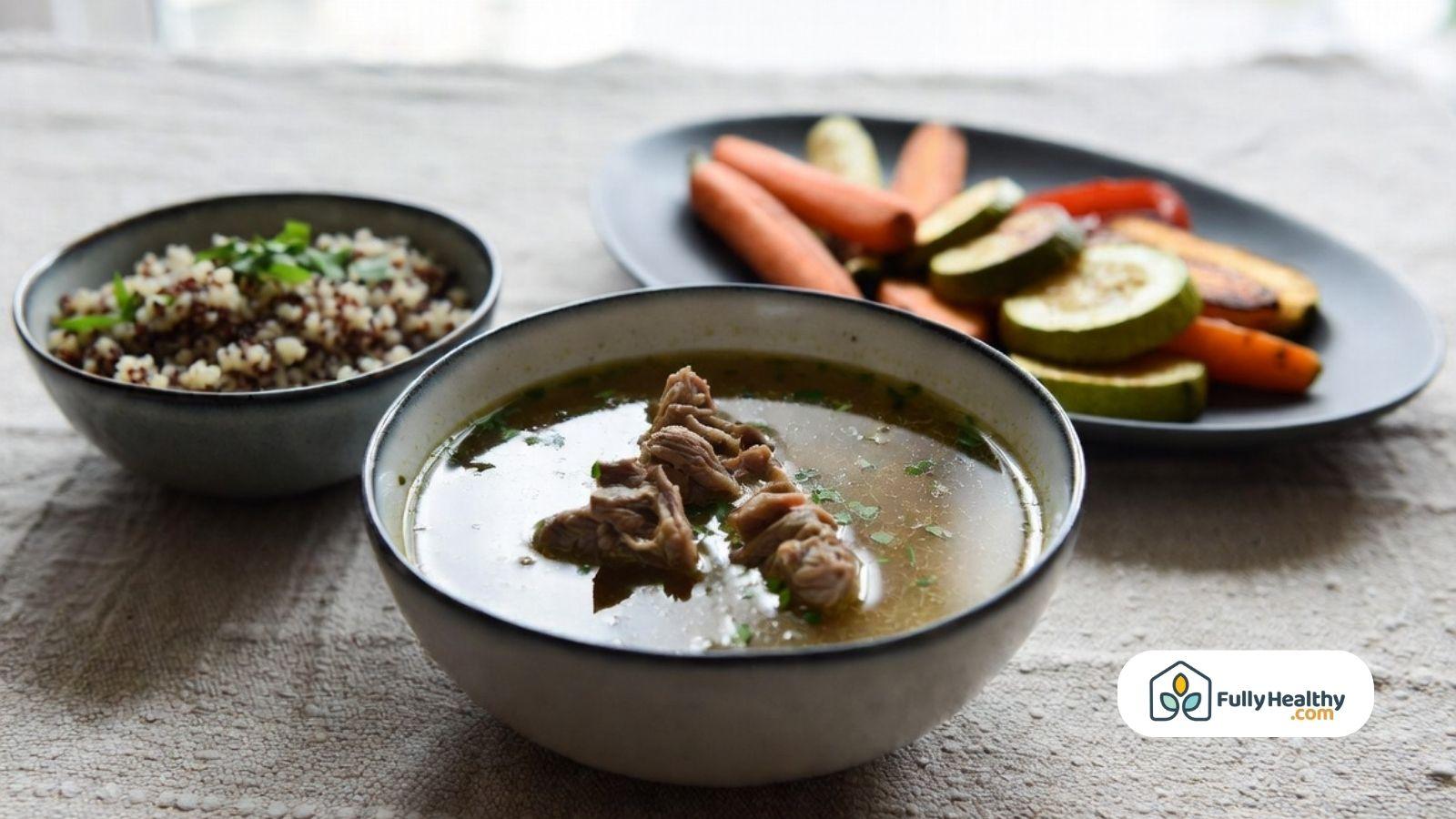 Bowl of broth with pieces of meat, served with quinoa and roasted vegetables on the side.