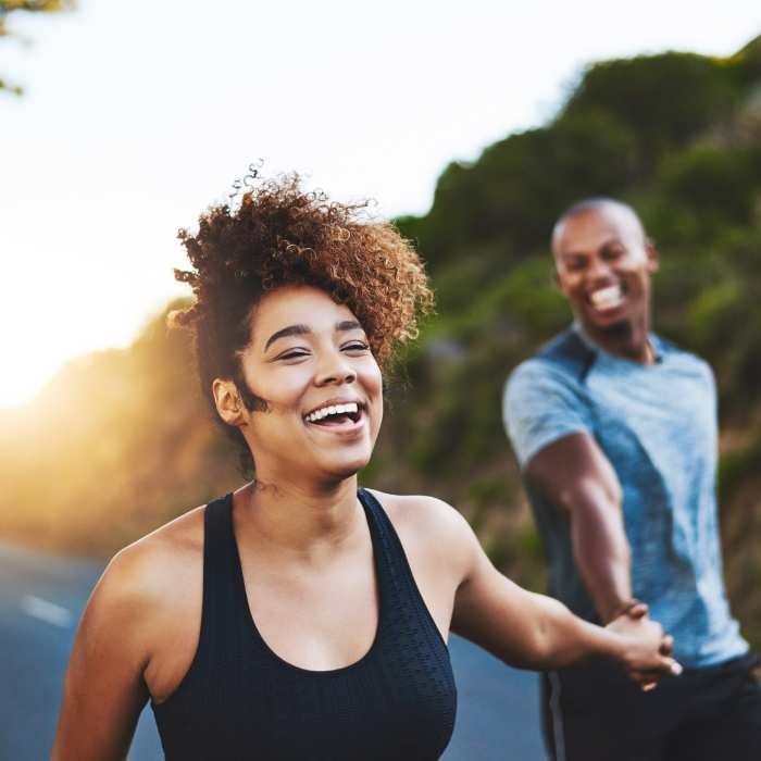 B complex vitamins - Couple laughing and holding hands while exercising on a road.