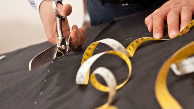 A Tailor using large fabric scissors to cut fabric used to make a suit.