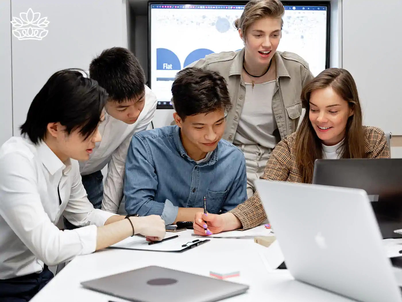 A group of five young, diverse professionals collaboratively working around a laptop in a well-lit office space, engaging in a productive team discussion. This scene depicts the dynamics of teamwork and effective communication. Gift boxes for colleagues, delivered with heart by Fabulous Flowers and Gifts.