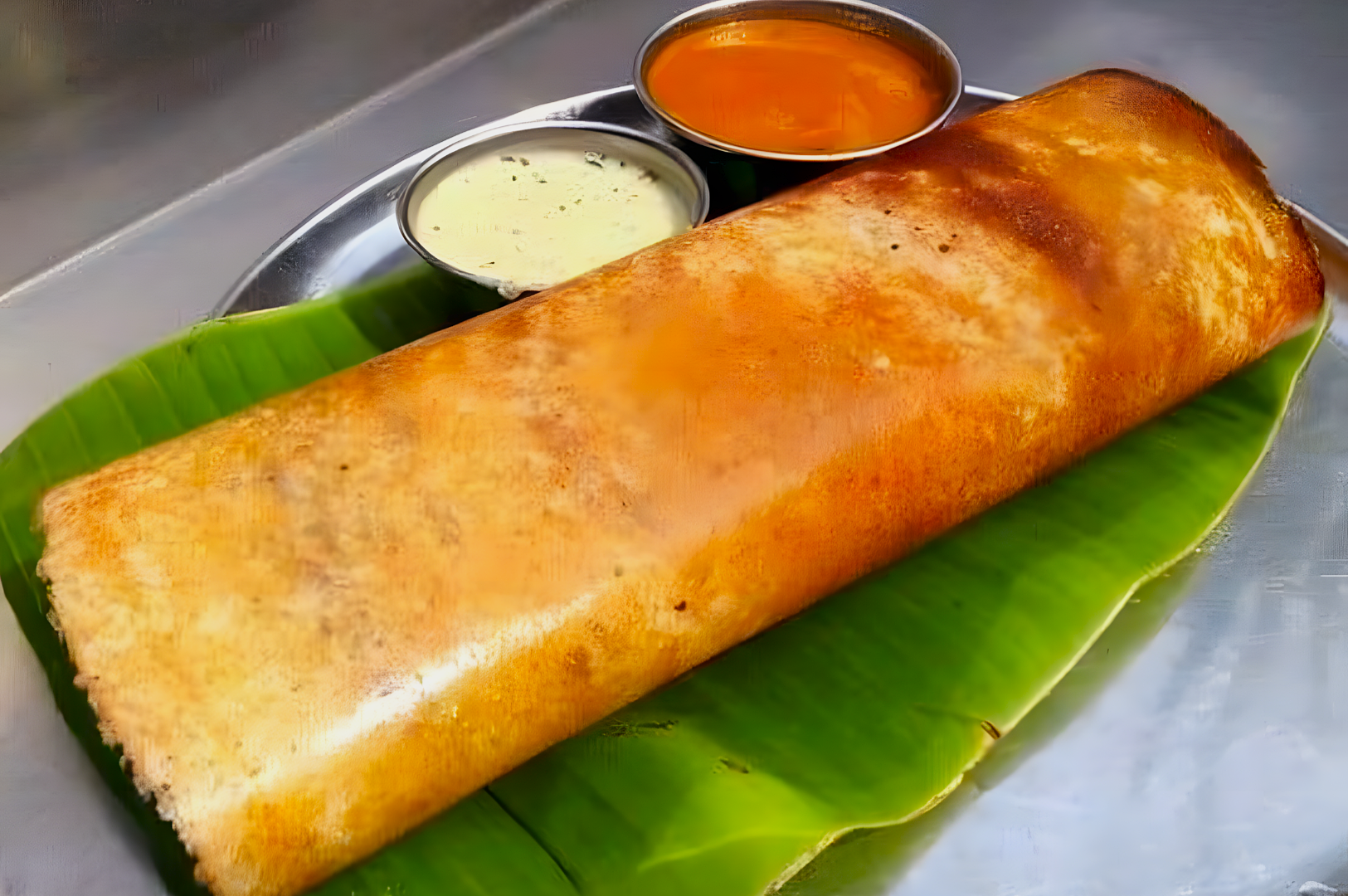 A crispy golden dosa rests on a banana leaf, accompanied by white coconut chutney and orange sambar. The setting is vibrant and appetizing.