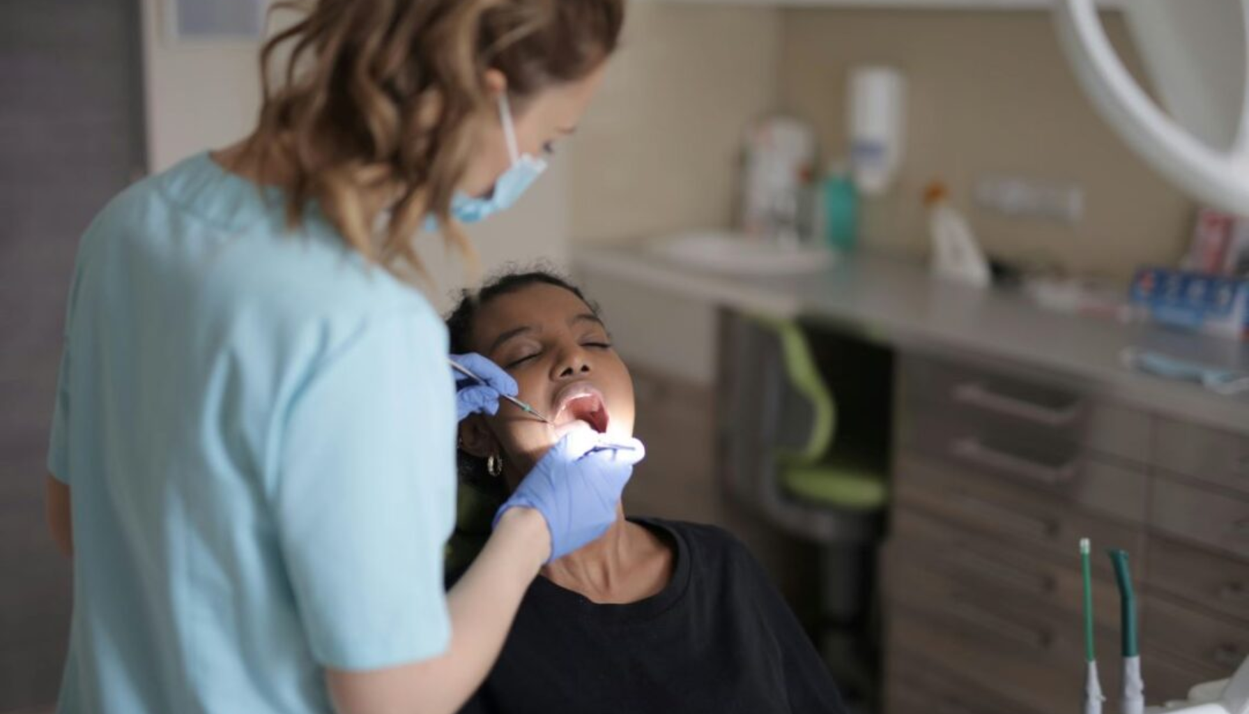 "Tannlege med hansker og munnbind undersøker pasients tenner med speil og instrumenter i tannlegekontor."