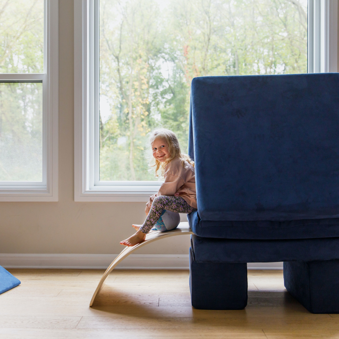 Girl in a Figgy play couch fort with a wobble board slide