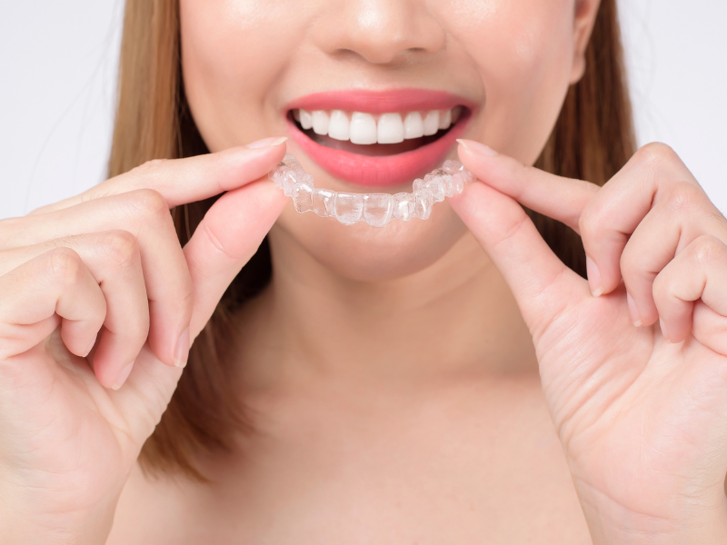 Image of someone holding up Invisalign aligners and smiling.