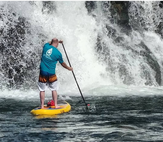 man paddling paddle board by waterfall