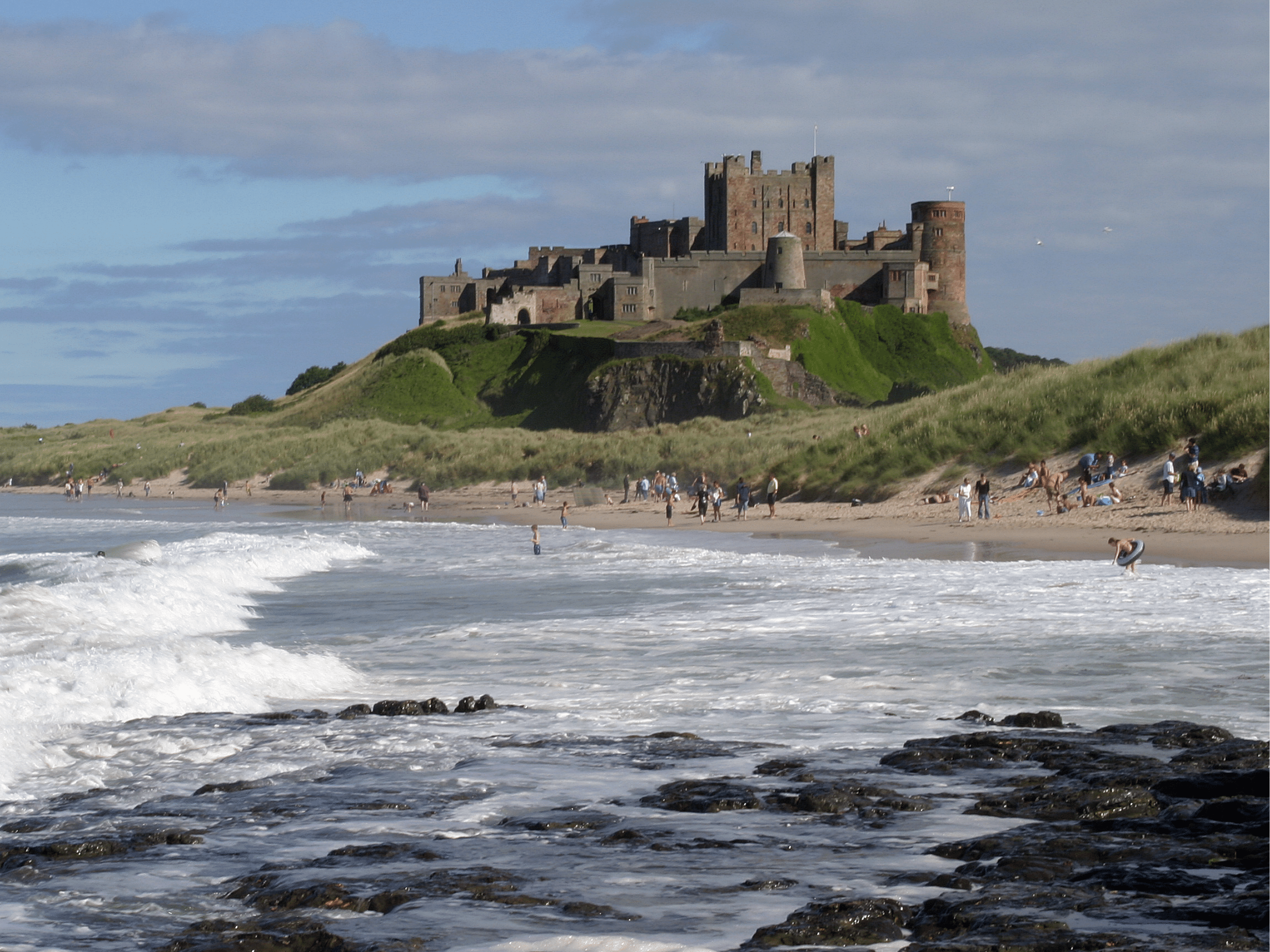 the beautiful and majestic Bamburgh Castle. people playing in the beach in front of the castle.
