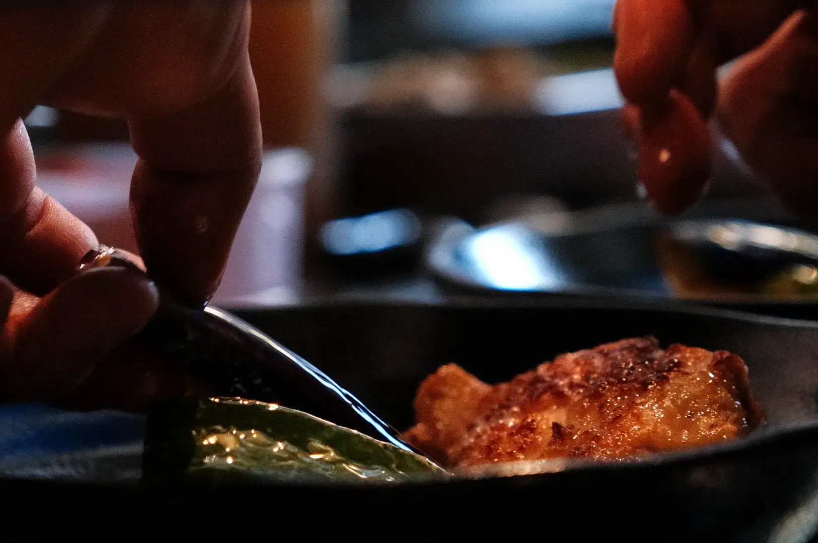 A close-up of hands using a fork to cut into a piece of food on a plate.