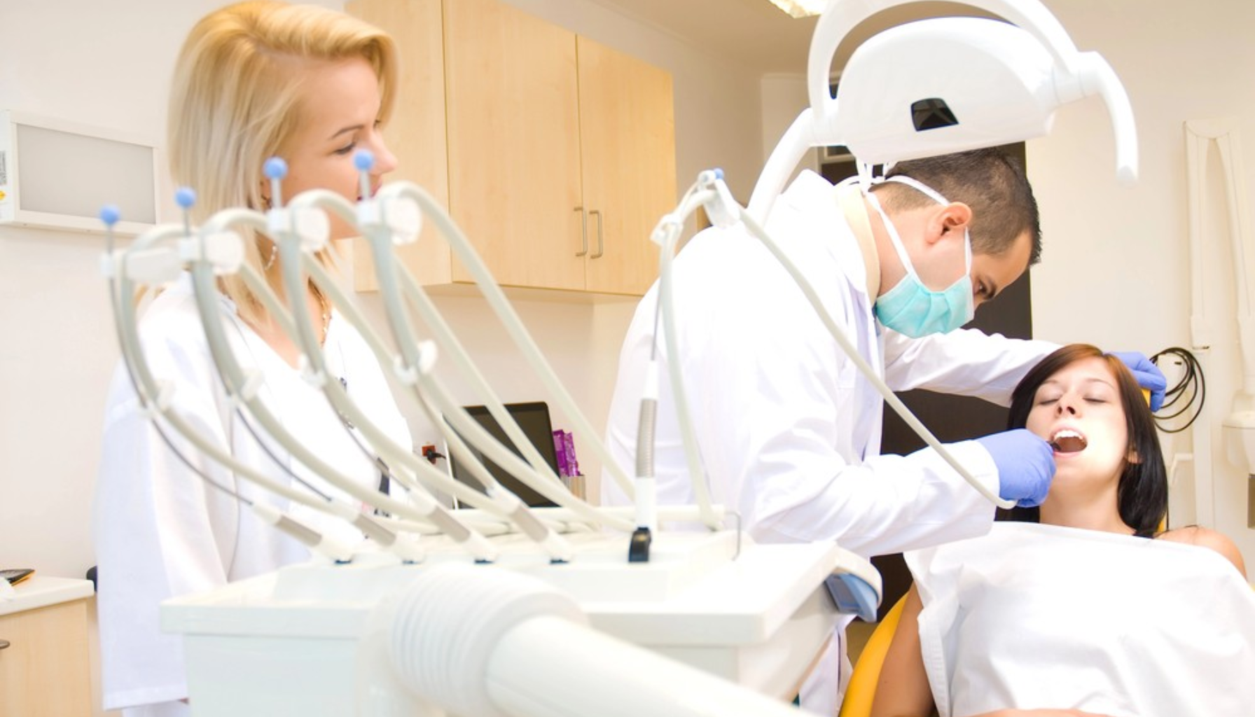 Helfo Frikort: Hva Pasienter Bør Vite om Dekning hos Tannlege 8 Tannlege behandler pasient i moderne klinikk mens assistent observerer med utstyr og sterkt lys over behandlingsstol under behandling
