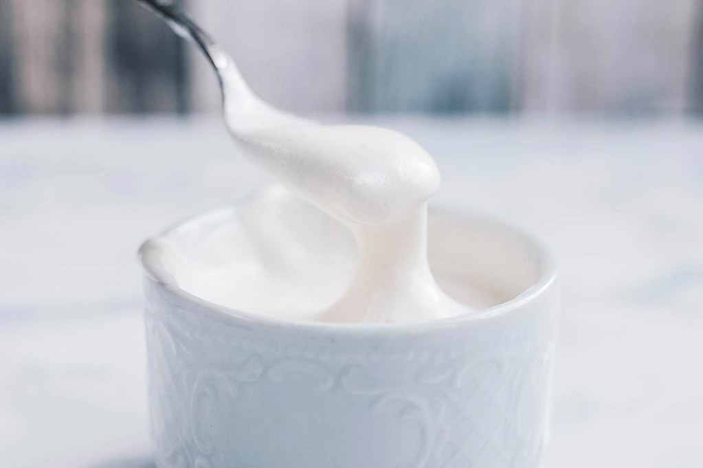 A spoonful of heavy cream being lifted from a container.