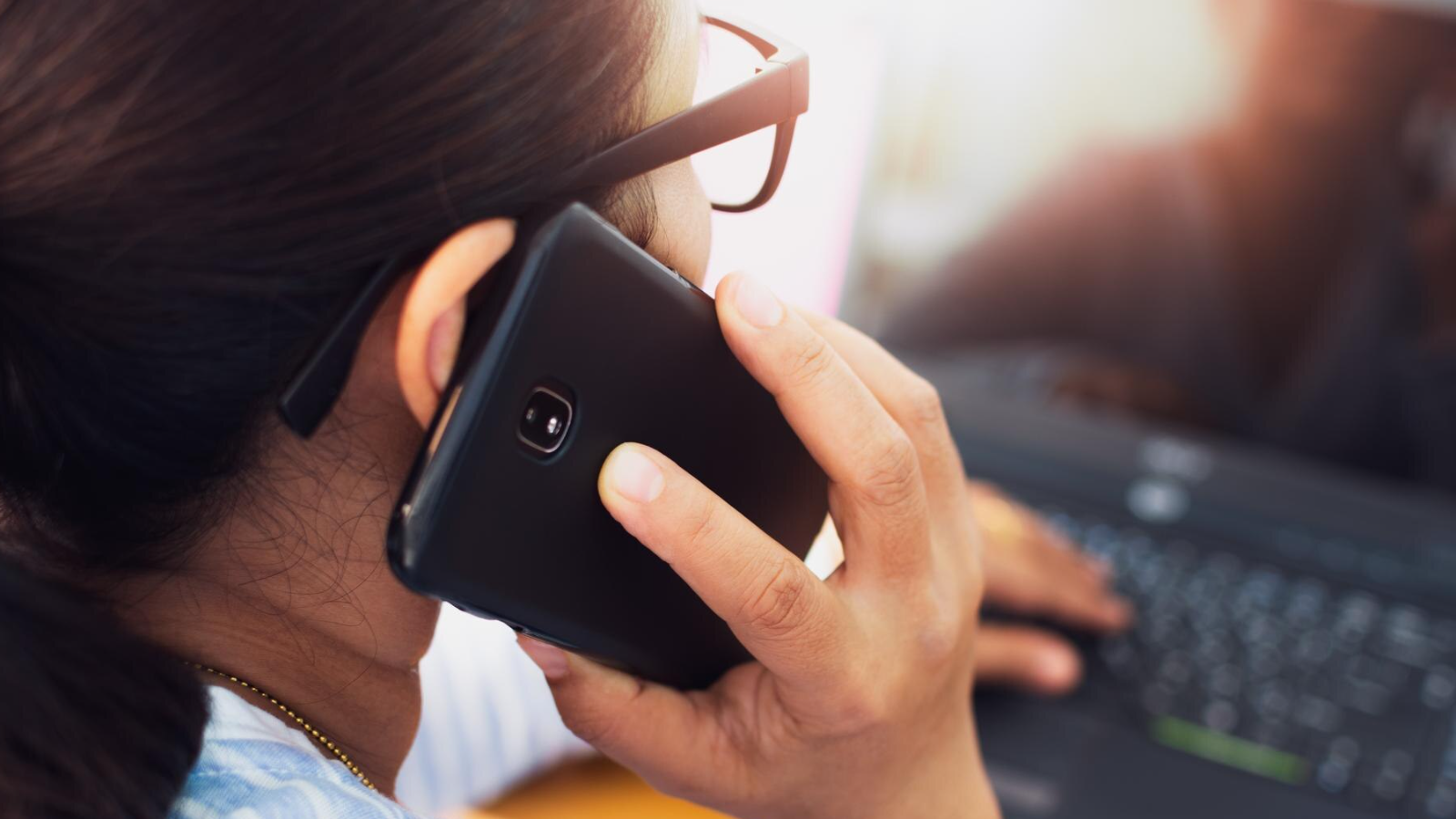 Woman on phone while working on laptop, reflecting improvements teams operator connect brings to Microsoft Teams Users.